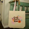 Beige tote bag with 'Cool People Sew' text and floral designs hanging on a green wooden chair.