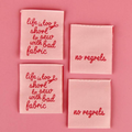 Four pink fabric patches with red embroidered text on a pink background