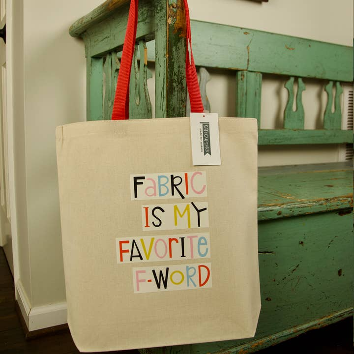 Beige tote bag with colorful text hanging on a green wooden bench.