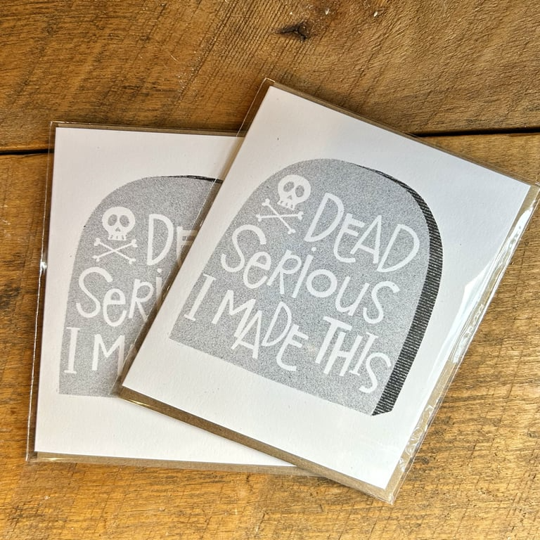 Two greeting cards with tombstone design and text on a wooden surface