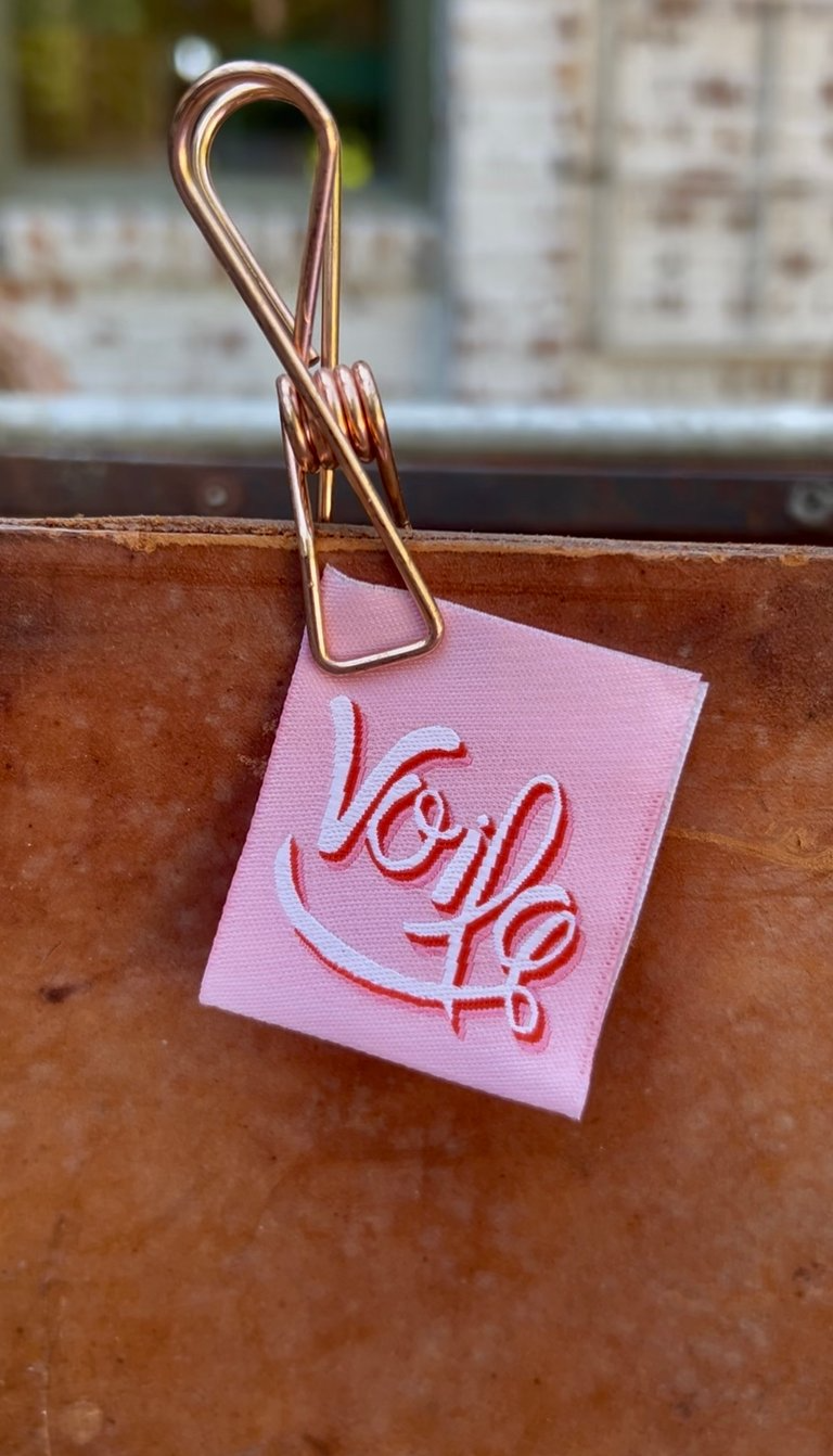 Pink paper with 'Voile' text attached to a wooden surface with a gold clip.