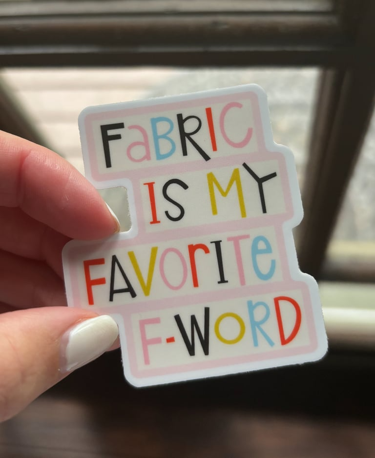 Sticker with colorful text held by a hand in front of a window.