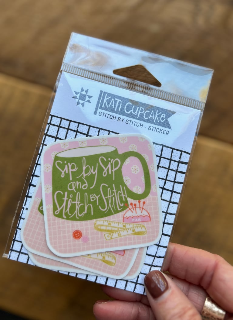 Packaged stickers with 'Kati Cupcake' branding held by a hand on a wooden surface.