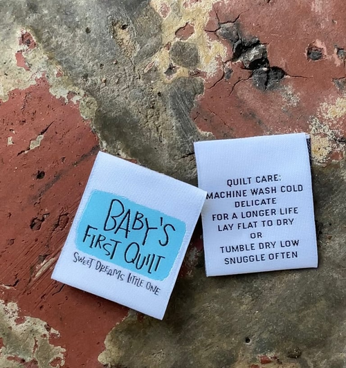 Two labels for a baby's first quilt on a textured surface