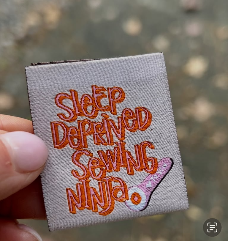 Embroidered patch with 'Sleep Deprived Sewing Ninja' text held by a hand against a blurred background.