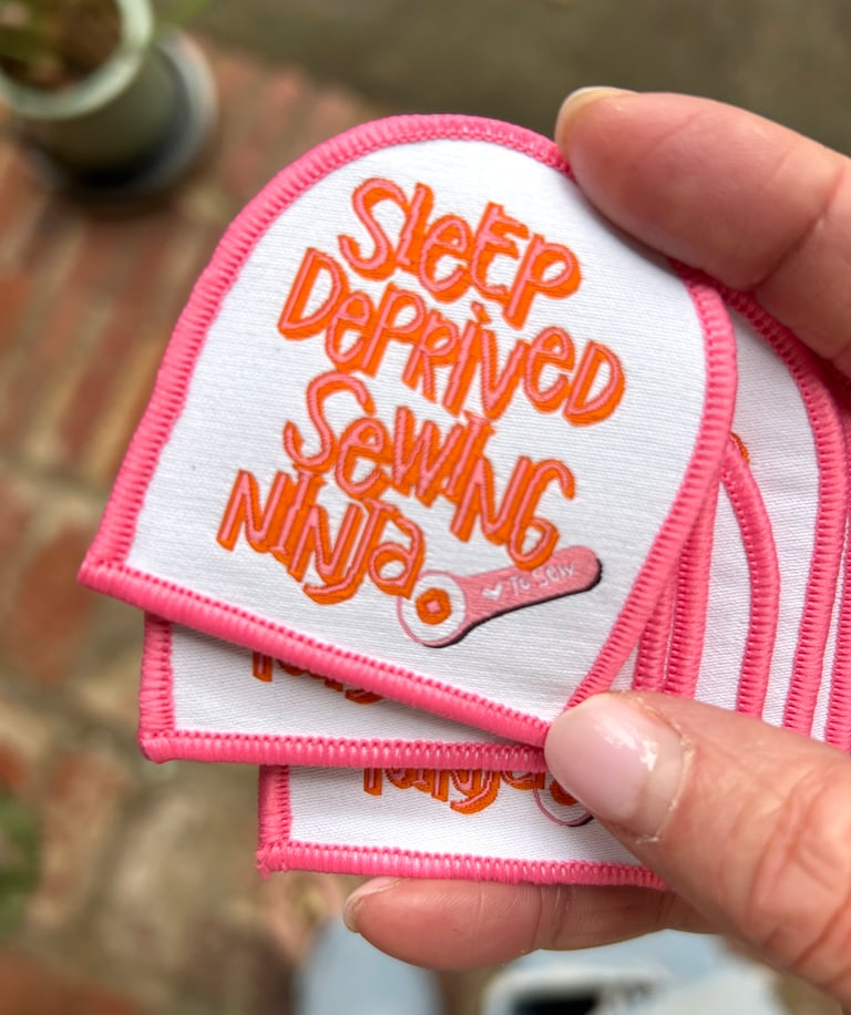 Embroidered patch with 'Sleep Deprived Sewing Ninja' text held by a hand.