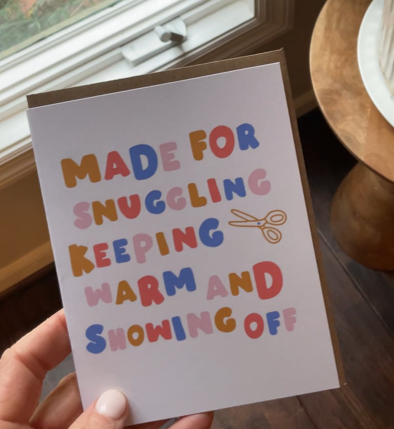 Card with colorful text held by a hand, with a window and wooden surface in the background.