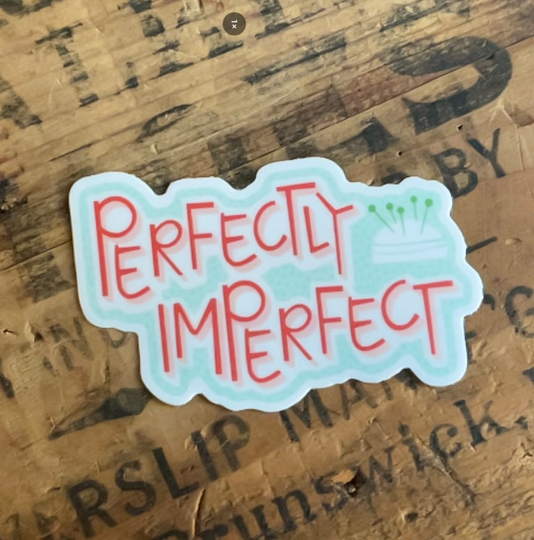 Sticker with 'Perfectly Imperfect' text on a wooden surface