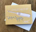 Greeting card with a sewing needle illustration and text on a wooden surface