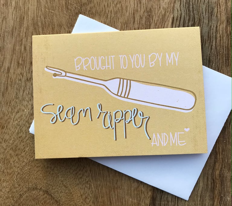Greeting card with a sewing needle illustration and text on a wooden surface