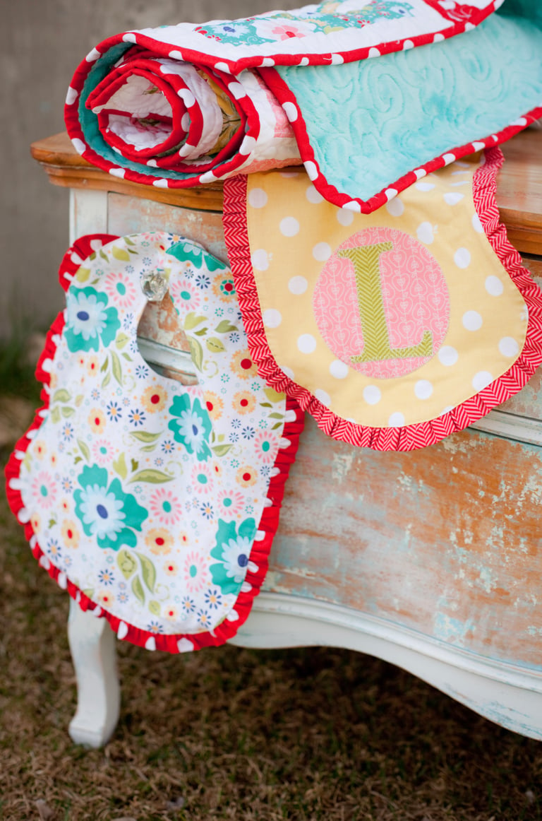 Colorful baby bibs with floral patterns and a letter 'L' on a wooden surface.