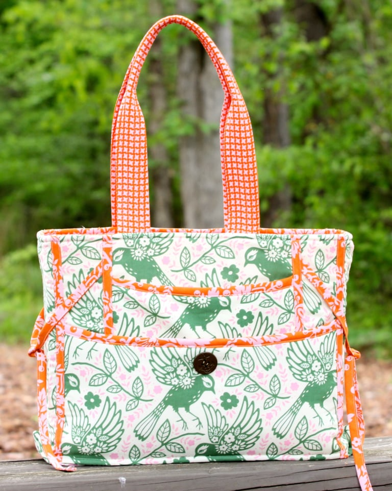 Fabric bag with green bird pattern and orange accents on a wooden surface with a blurred natural background