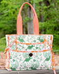 Fabric bag with green bird pattern and orange accents on a wooden surface with a blurred natural background