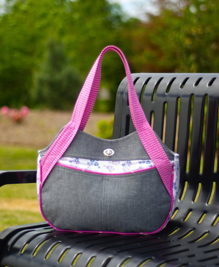 Gray handbag with pink straps on a black metal bench outdoors