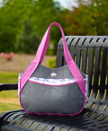 Gray handbag with pink straps on a black metal bench outdoors