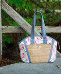 Handbag with floral pattern and woven design on a stone surface with greenery in the background
