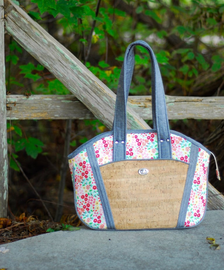 Handbag with floral pattern and woven design on a stone surface with greenery in the background