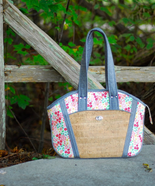 Handbag with floral pattern and woven design on a stone surface with greenery in the background
