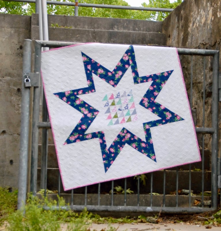 Quilt with star pattern hanging on a metal gate outdoors