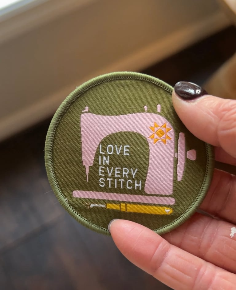 Embroidered patch with sewing machine design and 'Love in Every Stitch' text held by a hand.