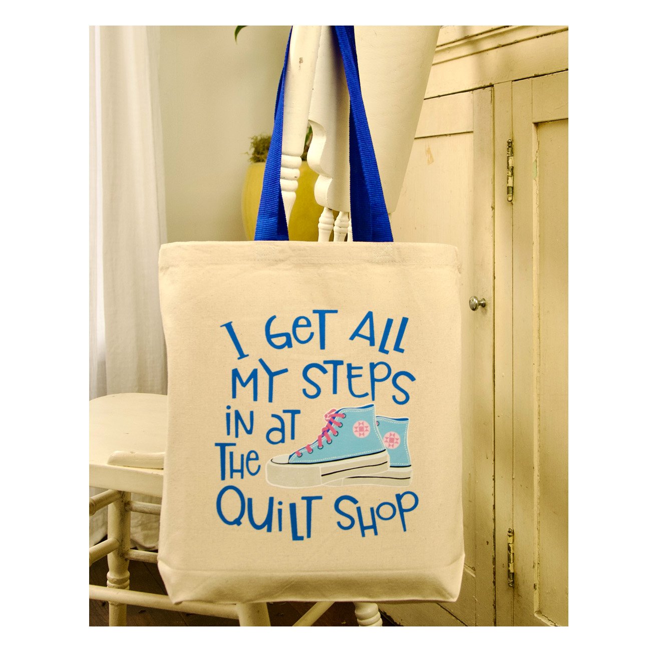 Beige tote bag with blue text and shoe graphic on a mannequin in a quilt shop setting.