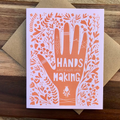 Greeting card with orange hand design and 'Hands are made for making' text on a wooden surface.