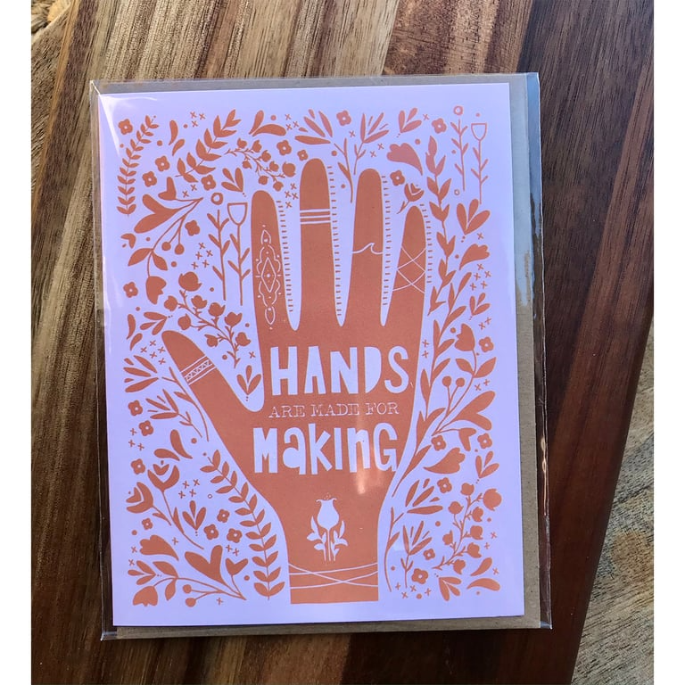 Card with decorative hand design and 'Hands are made for making' text on a wooden surface