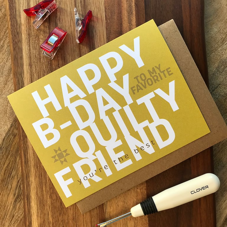 Greeting card with 'Happy B-Day to my favorite quilty friend' text on a wooden surface with sewing tools.