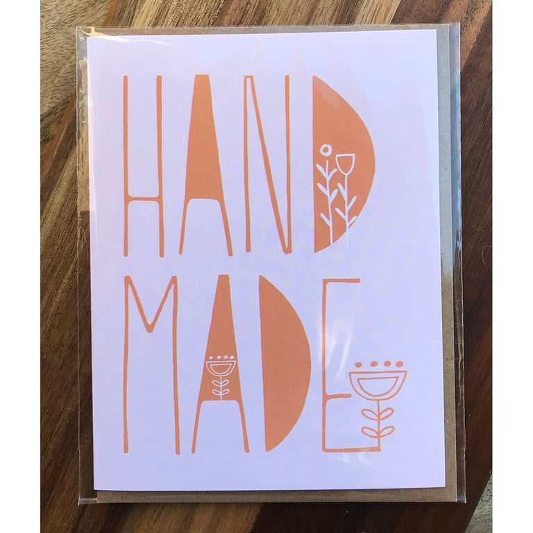 Card with 'HAND MADE' text and floral designs on a wooden surface