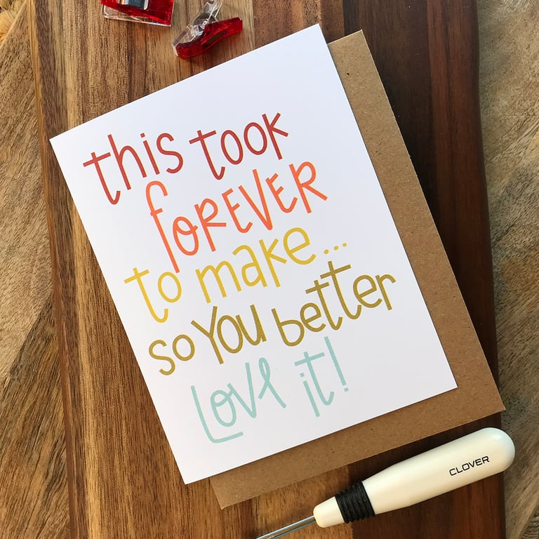 Card with colorful text on a wooden surface with a sewing tool.