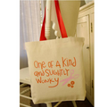 Beige tote bag with red handles and text 'One of a Kind and Slightly Wonky' on a chair.
