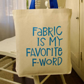 Beige tote bag with blue text 'Fabric is my favorite f-word' on a chair.