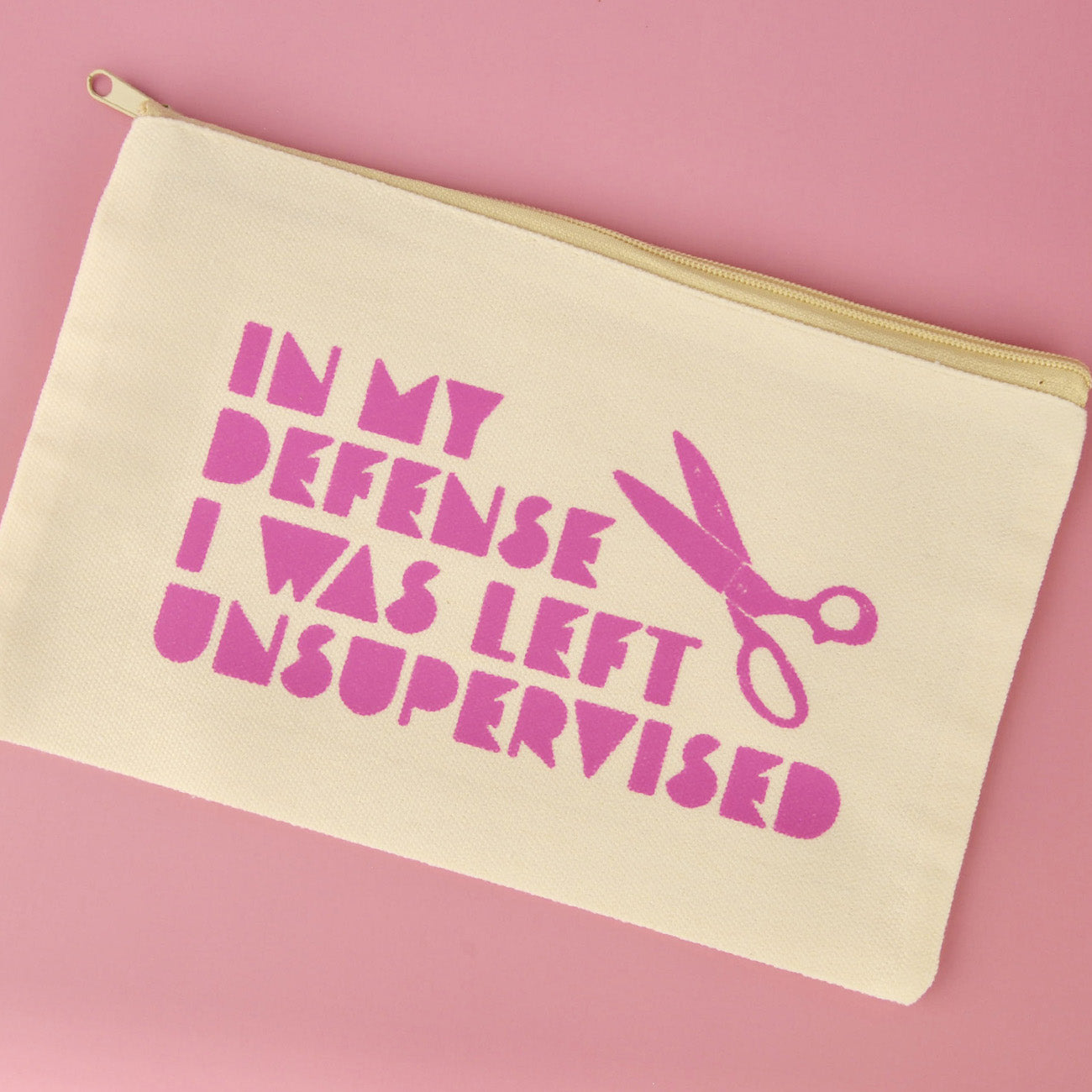 Beige pouch with pink text and scissors on a pink background