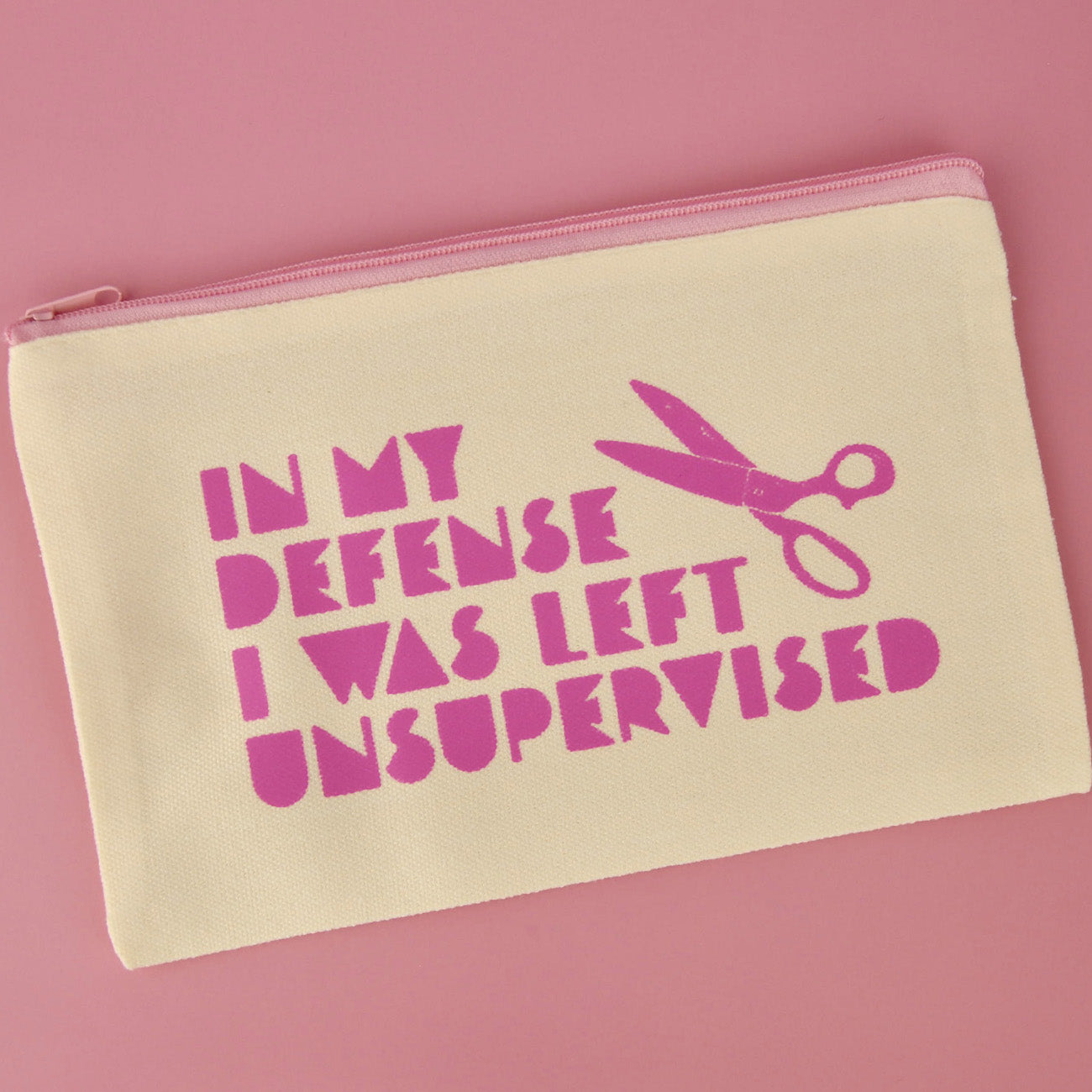 Beige pouch with pink text and scissors graphic on a pink background