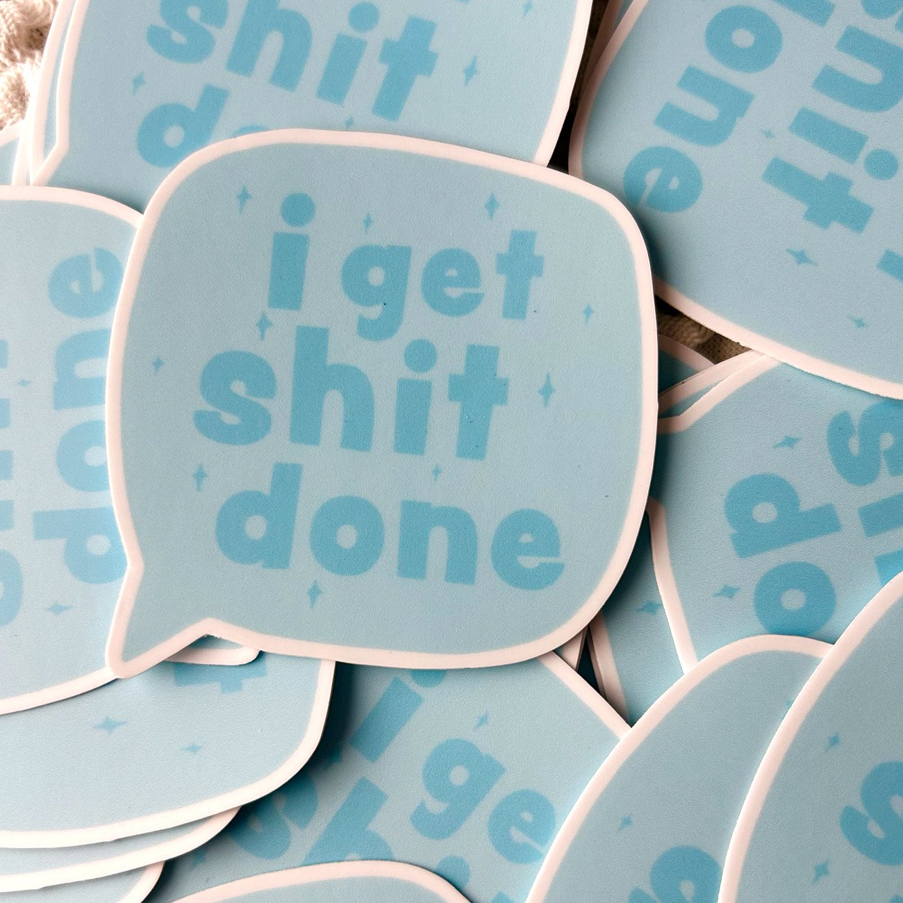 Stack of blue stickers with text 'i get shit done' on a matching background