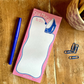Pink 'Sew Much To Do' notepad with iron illustration on a wooden surface with a pen and paper clips.