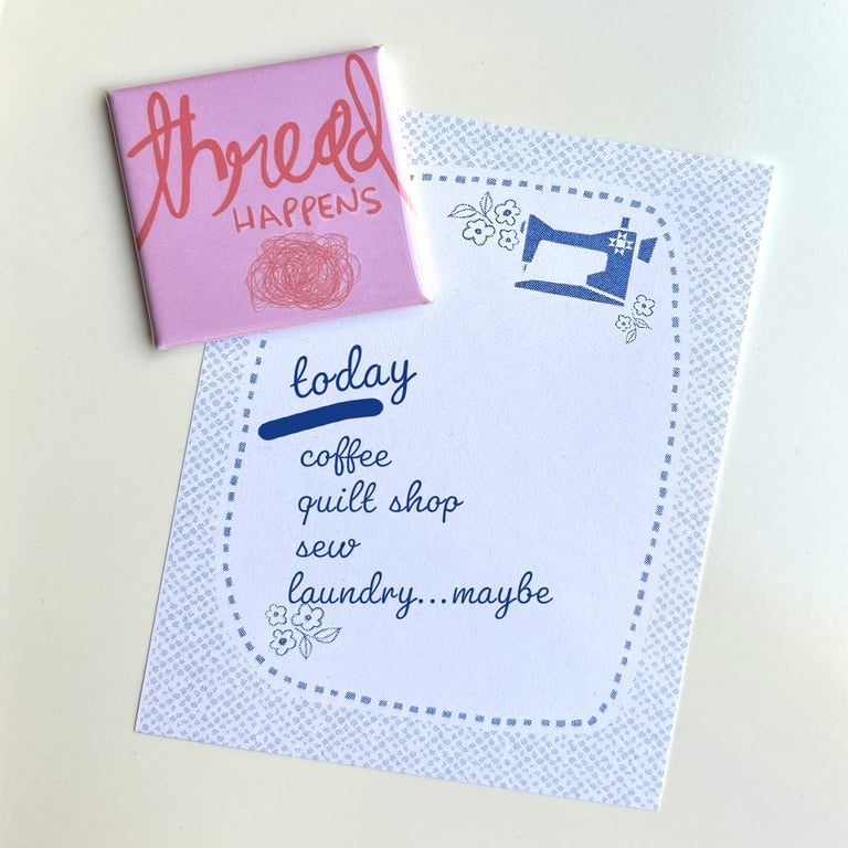 Notebook with sewing-themed cover and a pink notebook with 'thread happens' text on a light background.