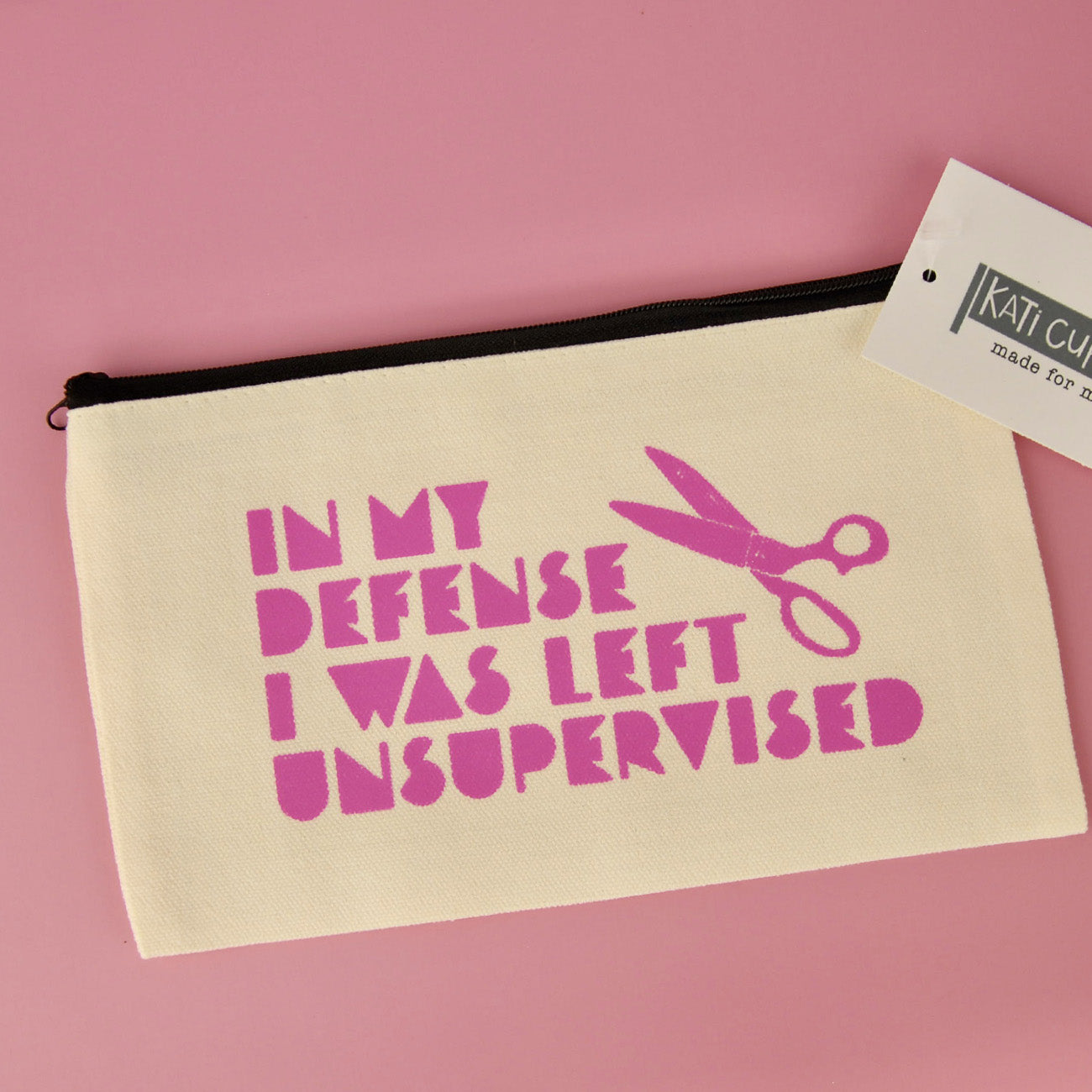Beige pouch with pink text and scissors graphic on a pink background